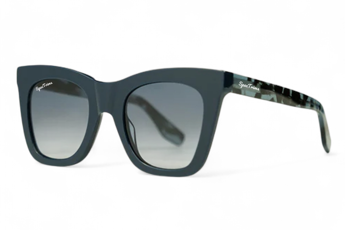 A pair of cat eye designer sunglasses with a dark teal-blue acetate frame, gradient blue lenses, and a blue-and-black camouflage pattern on the temple arm. The brand name 'SpecTrims' is visible on the temple.